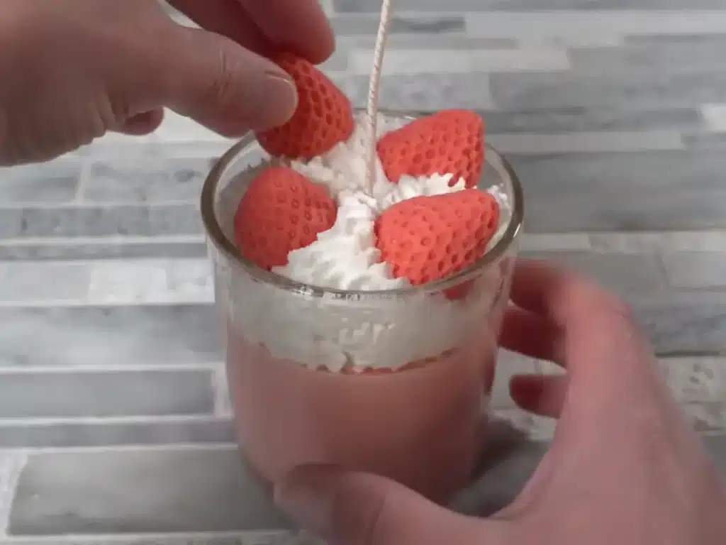 placing strawberry embed on top of candle with whipped top