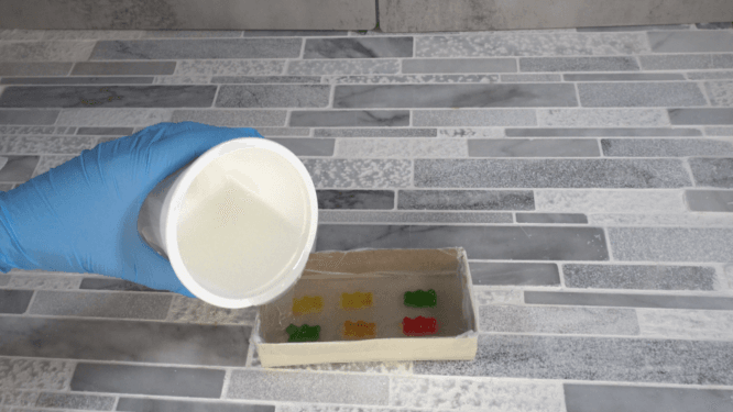 pouring silicone into box with gunny bears to make a mold